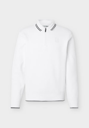 Λευκό μακρυμάνικο πόλο πουλόβερ με γιακά με μαύρες ρίγες και μαύρο τελείωμα στα μανίκια και το τελείωμα, με φερμουάρ μπροστά και διακριτικό λογότυπο στο στήθος.