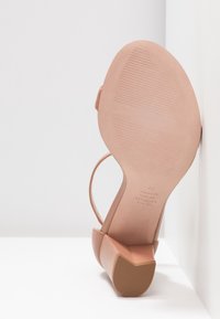 Sandal à talon haut nude avec un orteil arrondi, une bride de cheville, un dessus en cuir lisse, une semelle en caoutchouc texturé et un talon galbé.