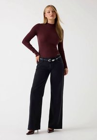 Bordeauxrød ribbet langærmet top kombineret med sorte vidde-bukser og et sort bælte. Mørke højhælede sko fuldender outfittet.