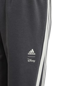 Pantaloni sportivi grigi in tessuto liscio, con strisce laterali bianche. Presentano i loghi ben visibili di adidas e Disney in bianco.