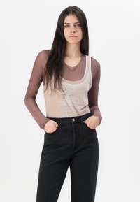 Beige tank top over a brown long-sleeve shirt, paired with high-waisted black pants. Smooth texture, simple design, minimal detailing.