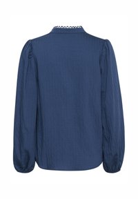 Blouse bleu marine à manches longues avec épaules bouffantes, tissu texturé, col montant à bord festonné et poignets élastiques.