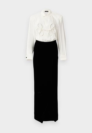 White long-sleeve blouse with loop accents at front, paired with a black velvet skirt, creating a sleek, elegant silhouette.
