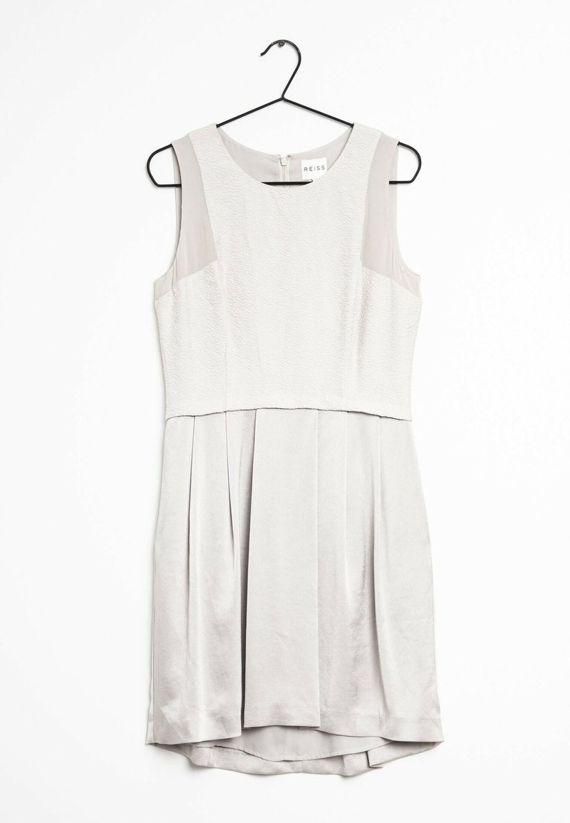 Robe blanche sans manches avec corsage texturé et jupe plissée suspendue sur un cintre noir sur fond blanc.