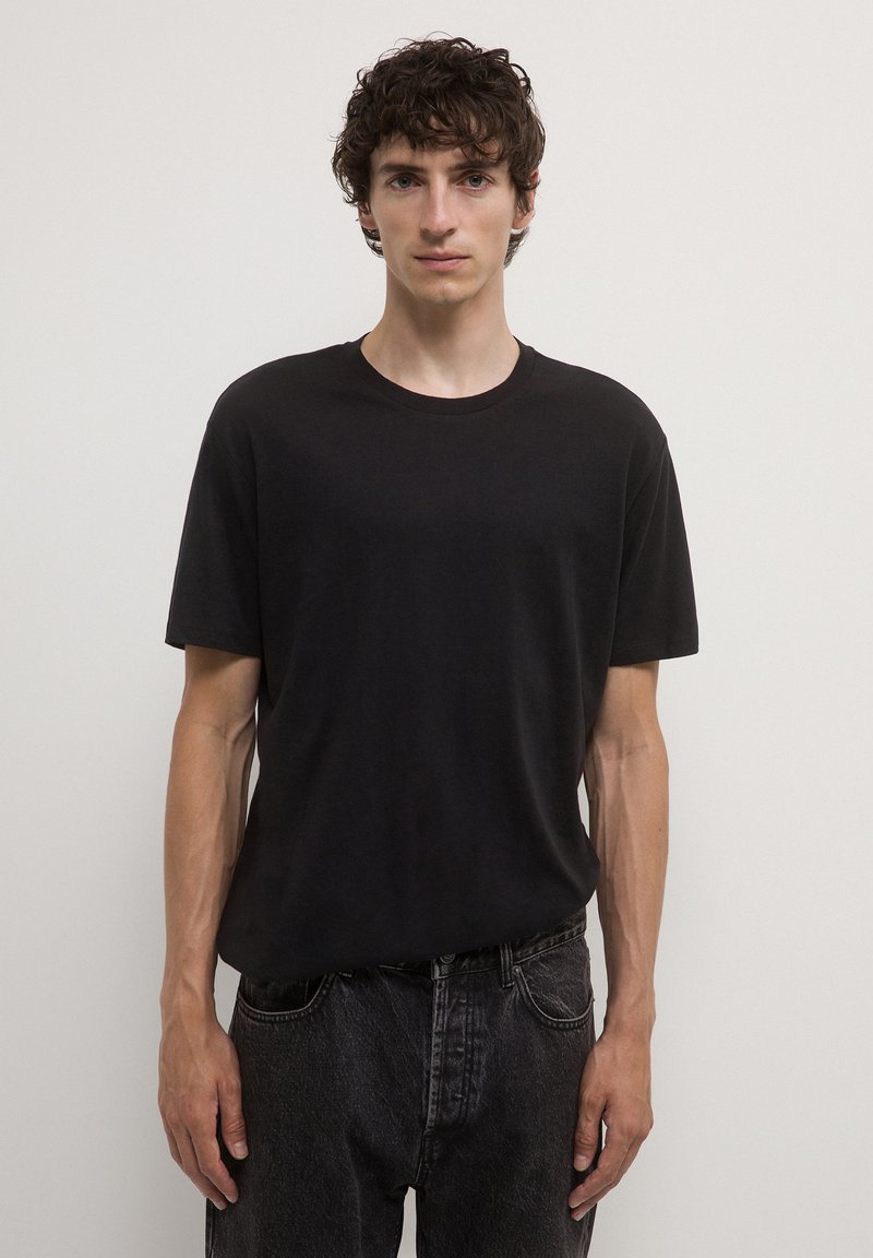 Maglietta nera in cotone con colletto a girocollo e maniche corte. Abbinata a jeans in denim scuri e sbiaditi. Design semplice e dal taglio rilassato.