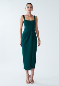 Turquoise aansluitende midi-jurk met een vierkante halslijn, brede bandjes, geplooid ontwerp en een voorste split. Gestyled met gouden sandalen met bandjes.