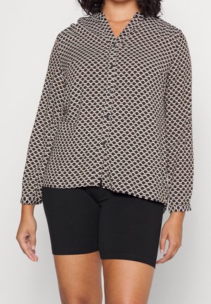 Kobieta ubrana w koszulę z długim rękawem z czarno-beżowym geometrycznym wzorem i jednolite czarne szorty.