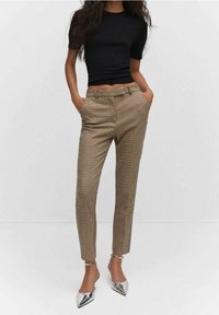 Pantalon beige à carreaux, coupe ajustée, ourlet retroussé à la cheville, poches avant, associé à un haut noir ajusté à manches courtes et des chaussures à talons argentées.