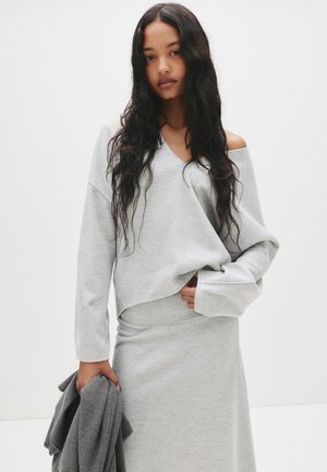 Grå loungewear sæt bestående af en blød, oversized sweater med V-udskæring og lange ærmer, parret med en matchende tætsiddende nederdel.