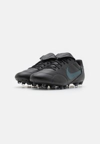Bottes de football noires avec une tige en cuir texturé, dotées d'un swoosh teal, d'un laçage à l'avant et d'une semelle extérieure en caoutchouc à crampons pour une meilleure traction.