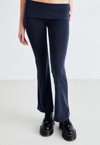 Sötétkék anyagból készült bővülő leggings széles derékrésszel, fekete fűzős platform csizmával párosítva, amelynek texturált talpa van.