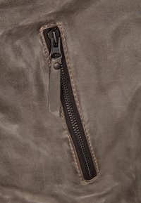 Taschina in pelle marrone con zip scura, dotata di accessori in metallo e dettagli di cucitura visibili su una superficie testurizzata.