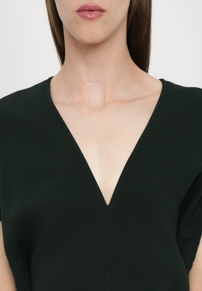 Prenda negra con escote en V y mangas cortas, textura suave y detalles de costura visibles en el frente. El diseño minimalista se centra en líneas limpias.