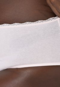 Světle růžové bavlněné spodní prádlo s krajkovým lemem v pase. Měkká textura, elastická látka a bezešvý design viditelný na tmavé pokožce.