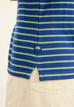 Tricou în dungi albastre și verzi, cu o f gaură laterală și o etichetă cu un desen de soare. Materialul pare moale și cu o textură netedă.