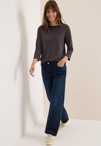 Haut à manches longues rayé en bleu marine et crème, associé à un jean évasé bleu foncé et des baskets beiges, sur un fond clair.