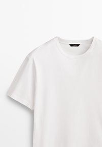 T-shirt blanc uni à manches courtes avec un col rond, étiquette de marque noire visible à l'intérieur du col sur fond blanc.