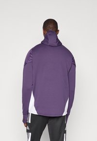 Lilla hoodie med høj krave, teksturerede ærmer og hvide sideaksenter. Lavet af blødt stof, med en afslappet pasform og lange ærmer.
