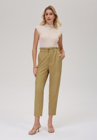 Beige ribbestrikket topp med ermer som går til skulderen, kombinert med olivengrønne høytaljede bukser med elastisk midje og frontknappdetaljer.
