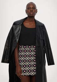 Schwarze Lederjacke mit breiten Revers, die über einem schwarzen Tanktop und einem gemusterten Minirock mit floralen Designs in Pink und Creme getragen wird.