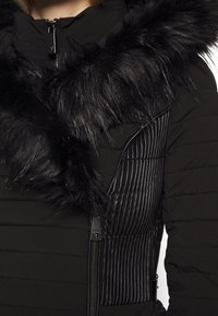 Czarna kurtka puchowa z kapturem z sztucznego futra. Posiada żebrowaną teksturę na bocznych panelach oraz zamek błyskawiczny, prezentując elegancki, zorganizowany fason.