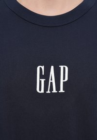 Μπλε ναυτικό T-shirt από βαμβάκι, με λευκό κεντητό λογότυπο "GAP" στο στήθος. Στρογγυλή λαιμόκοψη με ριμπ υφή.