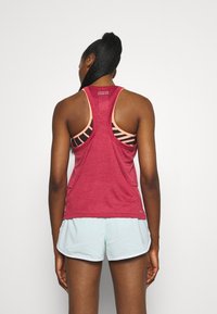 Camiseta atlética roja, transpirable, con diseño de espalda nadadora y textura de malla, combinada con pantalones cortos azul claro. Presenta un forro interior a rayas rosas.