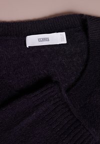 Schwarzer Strickpullover mit gerippten Bündchen und Halsauschnitt, versehen mit einem weißen Etikett, das "CLOSED" und "MADE IN TURKEY" trägt. Weiche Textur.