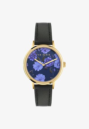 Zelta toņa pulkstenis ar melnu ādas siksniņu. Apaļā pulksteņa sejā ir tumši zila fona ar purpursarkanām ziedu rotām. Vienkāršas stundu un minūšu rādītājs.