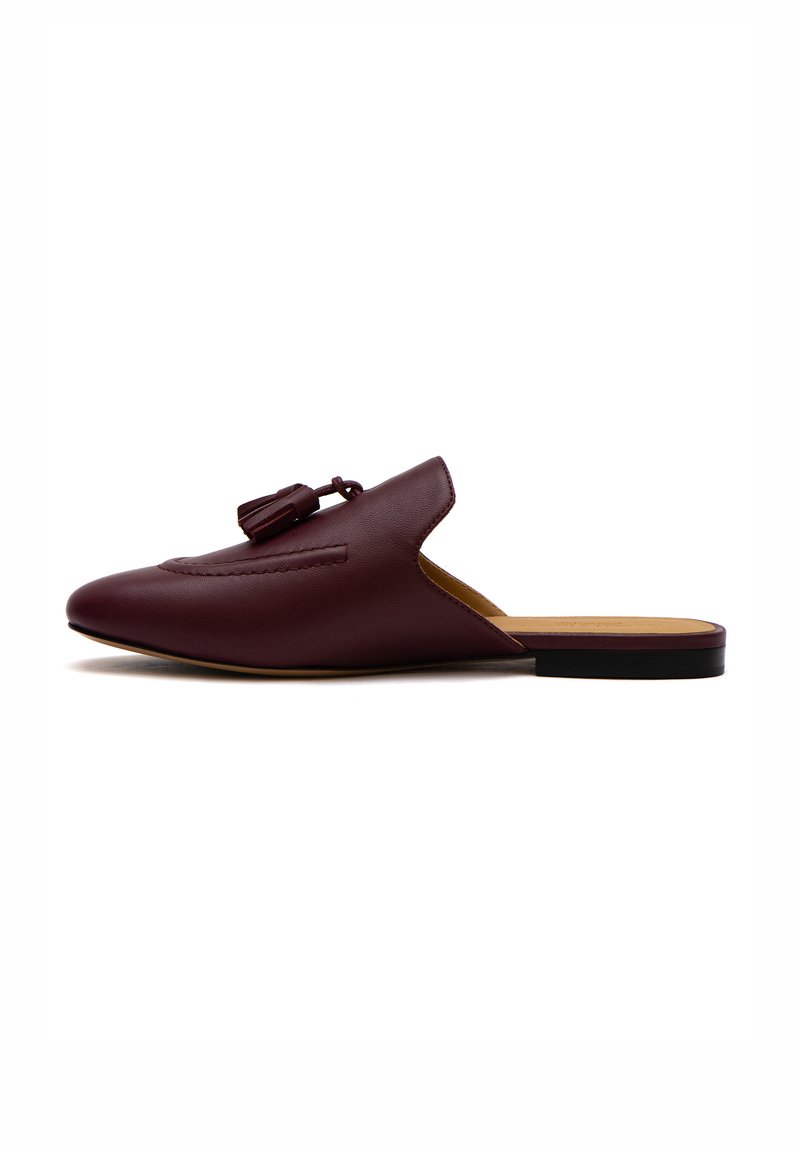 Mule in pelle bordeaux con punta affusolata, nappina decorativa e apertura sul retro. Presenta un tacco basso e piatto e dettagli cuciti lungo la parte superiore.