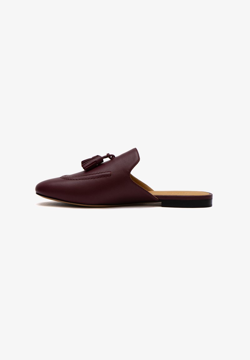 Mule in pelle bordeaux con punta affusolata, nappina decorativa e apertura sul retro. Presenta un tacco basso e piatto e dettagli cuciti lungo la parte superiore.