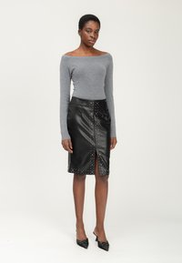 Grijze off-shoulder trui, gecombineerd met een zwarte leren kokerrok met verticale studaccenten en een split aan de voorkant. Geheven schoenen maken de look compleet.
