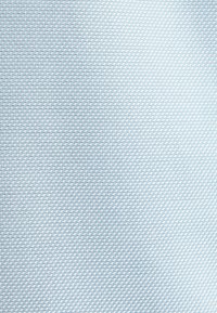 Tissu bleu clair avec un motif géométrique répétitif à petite échelle de formes imbriquées créant une surface texturée.