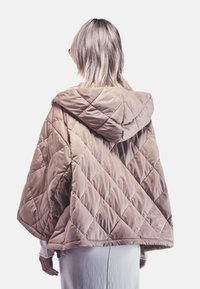 Gequilted beige trenchcoat met een losse pasvorm, voorzien van een ruitpatroon en een gladde, glanzende textuur. De zoom en mouwen hebben minimale details.