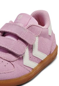 Różowy zamszowy tenisówka z białymi akcentami, dwoma paskami na rzep, perforowanymi detalami i gumową podeszwą, z zaokrąglonym noskiem i wyściółką zapewniającą wygodę.