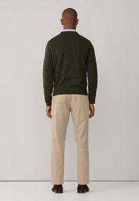 Dunkelgrüner Strickpullover mit Rundhalsausschnitt, kombiniert mit hellbeigen Hosen und braunen Schuhen. Glatte Textur und klassischer Schnitt.