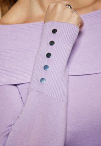 Top lavandă cu umeri goi, textură cu ribbing și mâneci lungi, având cinci butoane metalice pe manșetă. Design moale, ajustat.