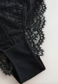 Black lace lingerie with floral patterns and scalloped edges on a plain light background.