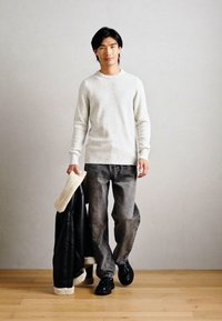 Λευκός υφασμάτινος σκούφος, γκρι ξεθωριασμένα τζιν και μαύρα δερμάτινα παπούτσια. Κρατώντας ένα μαύρο δερμάτινο μπουφάν με λευκή γούνα.