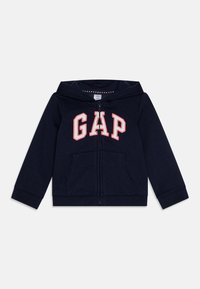 Hanorac cu fermoar de culoare bleu marin, cu logo-ul "GAP" în alb și roșu. Include buzunare frontale și manșete plisate. Fabricat dintr-un material moale și texturat.