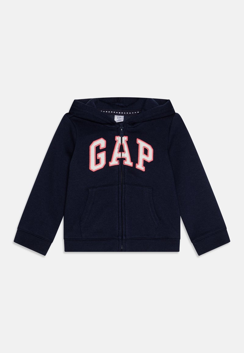 Hanorac cu fermoar de culoare bleu marin, cu logo-ul "GAP" în alb și roșu. Include buzunare frontale și manșete plisate. Fabricat dintr-un material moale și texturat.