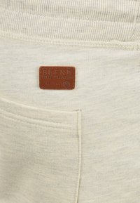 Pantalones de chándal color crema con una cinturilla acanalada, una pequeña etiqueta de cuero con "BLEND GLOBAL JEANMAKERY" y un bolsillo lateral.