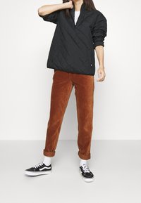 Sort quiltet pullover med halvlukning, parret med rustfarvede fløjlbukser og sorte sneakers. Har rullede manchetter og tekstureret stof.