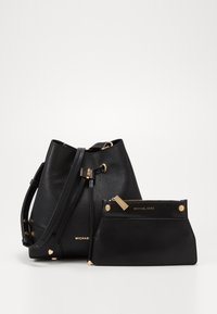 Bolso de cubo de cuero negro con un acabado texturizado, que presenta herrajes dorados y cierre de cordón, acompañado de un pequeño clutch negro.