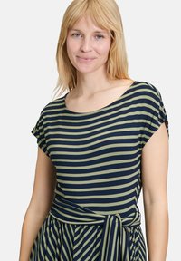 Pasiasta sukienka wykonana z lekkiego materiału; ma krótkie rękawy, okrągły dekolt oraz wiązany detal w talii z naprzemiennie rozmieszczonymi niebieskimi i oliwkowymi paskami.