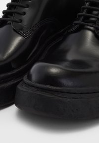 Chaussures en cuir noir avec une finition brillante, présentant un bout arrondi et une semelle en caoutchouc épaisse. Design à lacets avec des détails de couture contrastants.