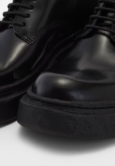 Black leather shoes with a glossy finish, featuring a rounded toe and thick rubber sole. Lace-up design with contrasting stitching details.