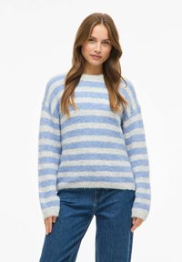 Jersey de rayas azules y blancas con una textura suave y esponjosa, cuello redondo y un ajuste ligeramente holgado, combinado con vaqueros de denim.