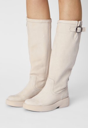 Bottes en cuir beige jusqu'aux genoux avec une texture lisse, des coutures subtiles et un détail de boucle sur le côté. Semelle épaisse de couleur crème.
