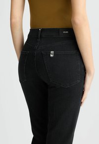 Mustad denim teksad, millel on sobiv disain, tagakülgedel taskud ja bränditud vöökoht. Materjal on sujuva tekstuuriga ja kergelt veniv.